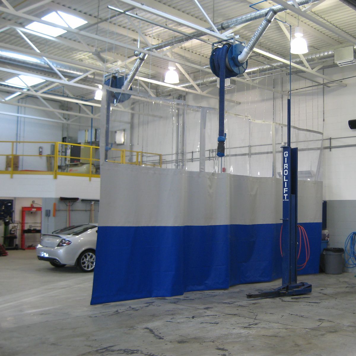 Car wash bay with blue and gray curtains, overhead hoses, and a car inside.