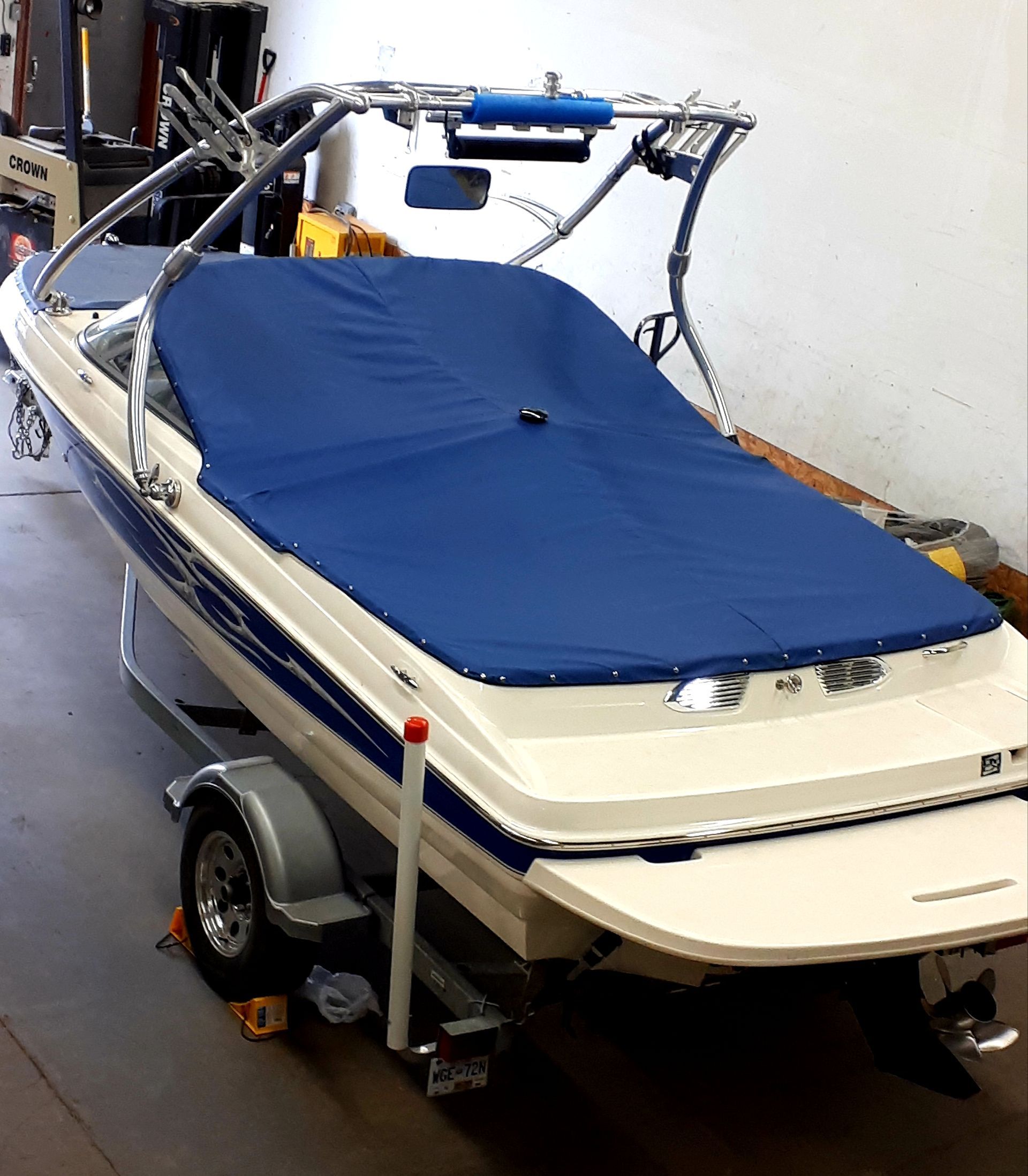 Blue covered white and blue boat on trailer, inside a garage.