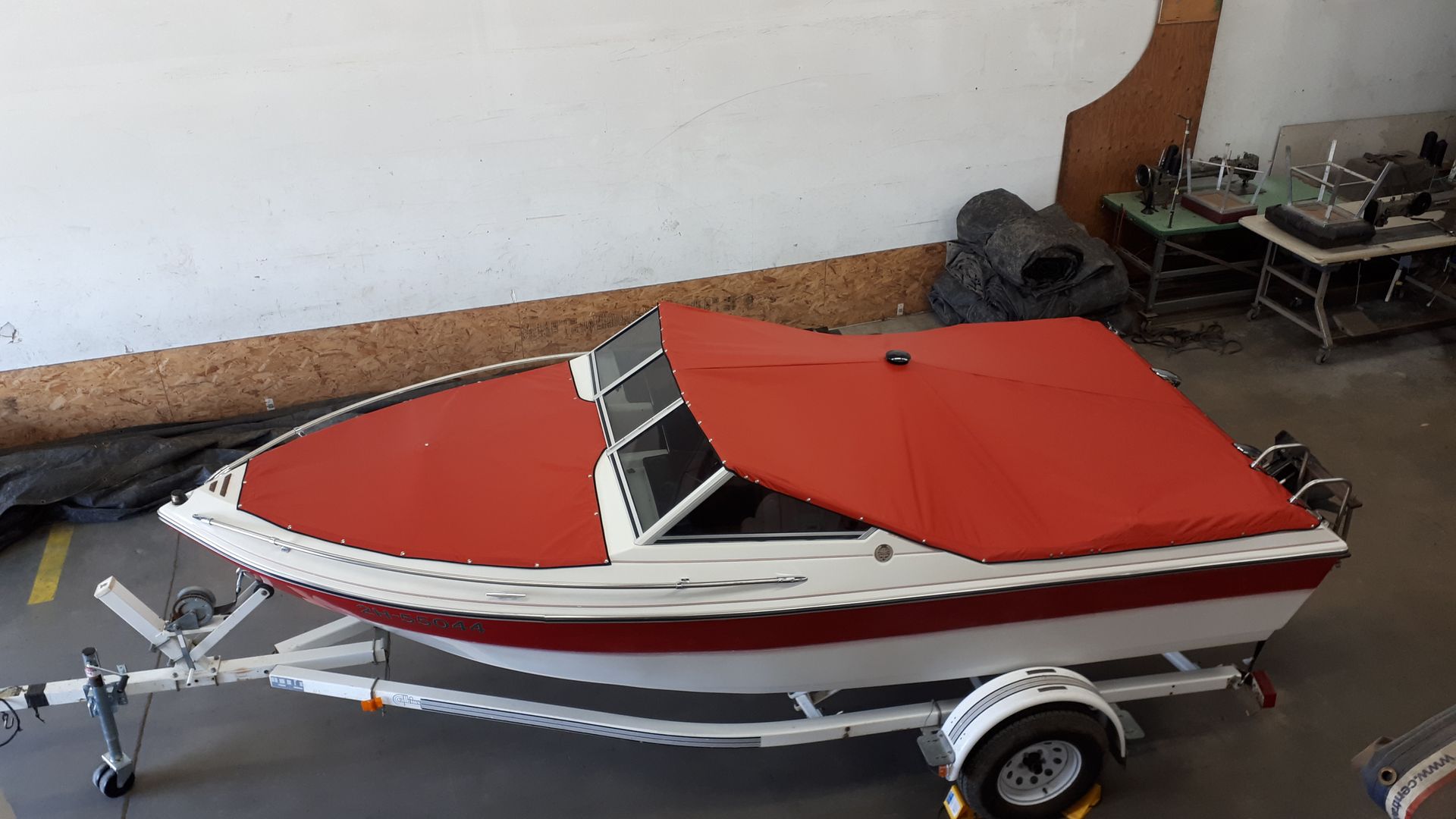 Red and white motorboat on a trailer, covered with a red tarp.