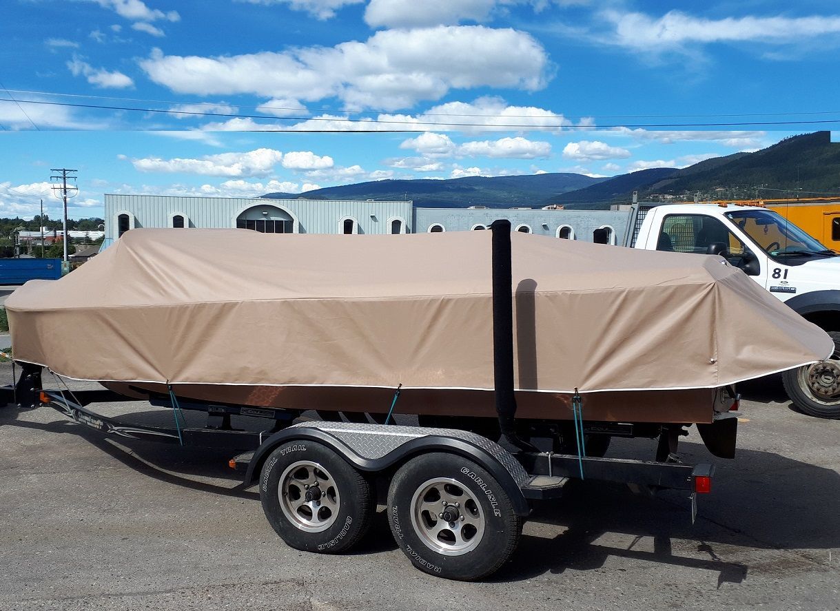 Tan boat covered on a trailer, parked outside on a sunny day.
