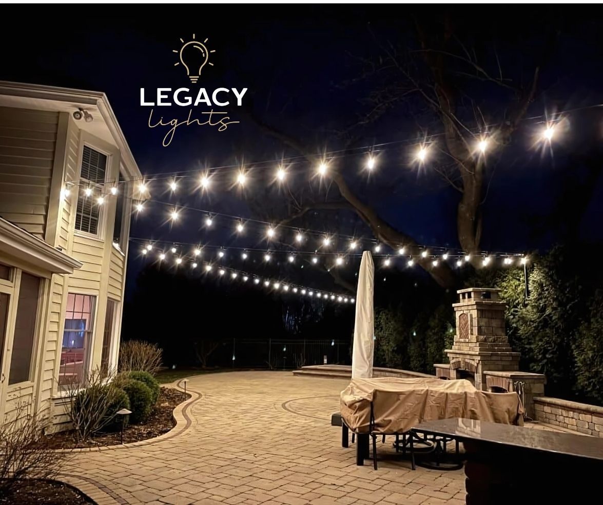 Outdoor patio with string lights illuminating a backyard at night. A house and stone fireplace are visible.