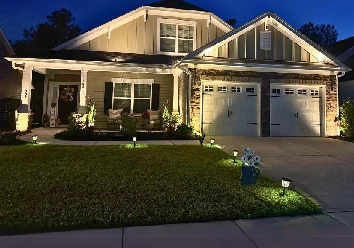 Night view of a house with exterior lighting, including a lawn and garage.
