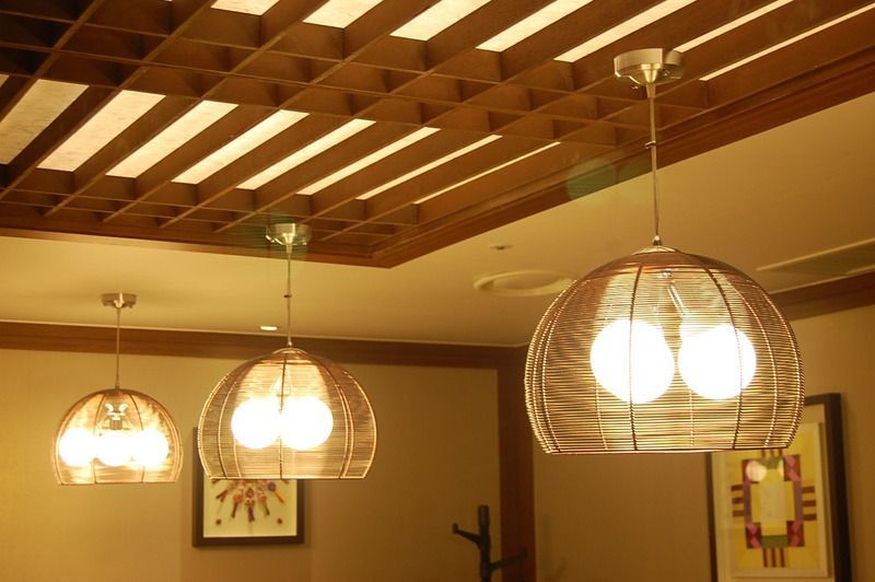 Three pendant lights with woven shades hanging from a grid ceiling.