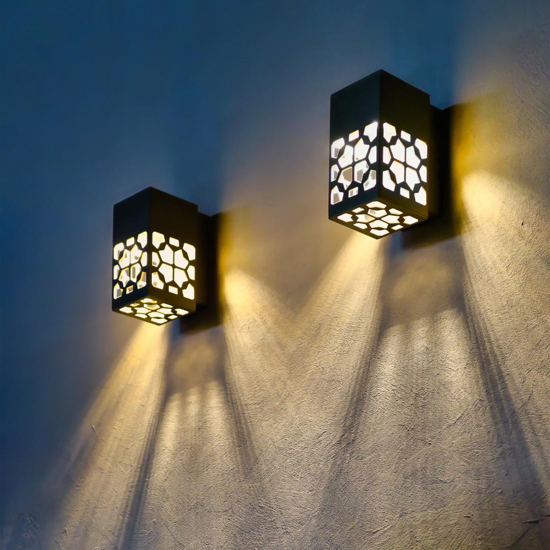 Two outdoor sconce lights with intricate patterns casting shadows on a blue-grey wall.