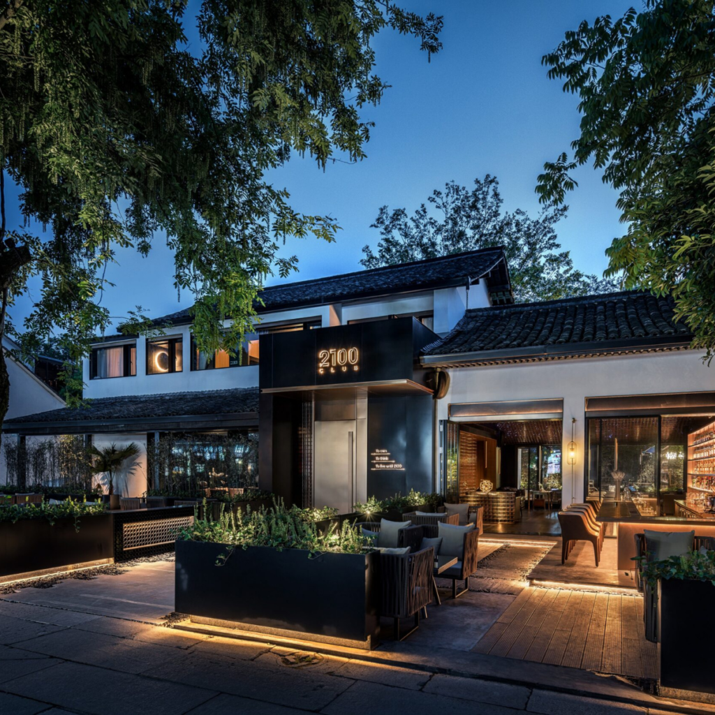Restaurant exterior at dusk with illuminated path and greenery.