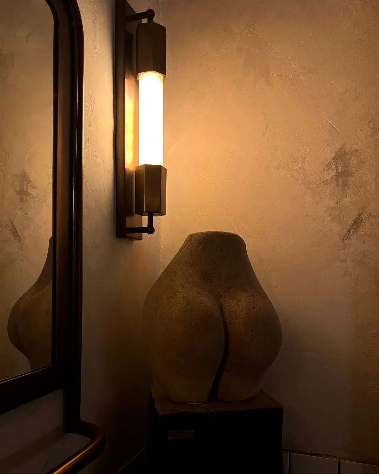 Aesthetic bathroom setup with a butt-shaped sculpture and a modern wall-mounted light fixture.