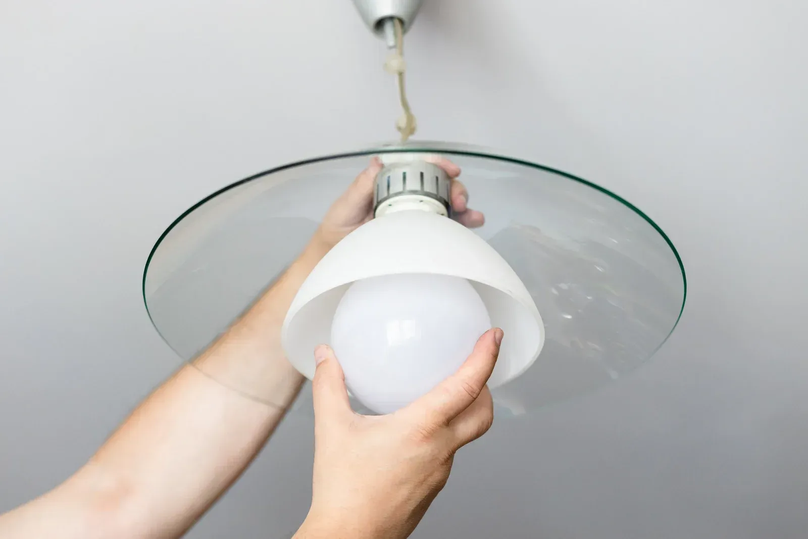 Person replacing a lightbulb in a white lampshade, attached to a ceiling.