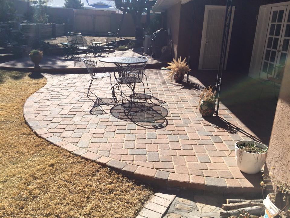 Brick patio with wrought iron furniture, next to brown grass and a house.