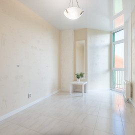 Bright empty white room with tiled floor, tall windows, and a small table with a plant.