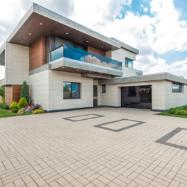Modern two-story house with a balcony and large paved driveway under a bright sky