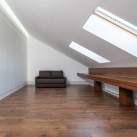 Minimal attic room with sloped skylights, wood floor, gray sofa, and long wooden table