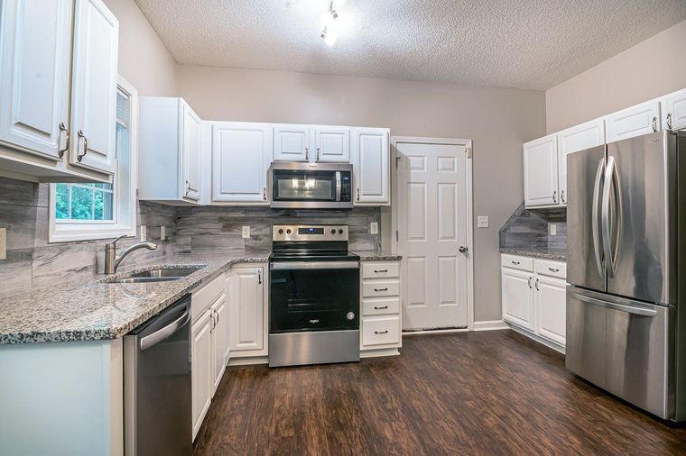 Bright modern kitchen with white cabinets, stainless steel appliances, granite counters, and dark wood flooring