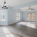 Empty bright living room with light blue walls, large windows, gray flooring, and ceiling fans