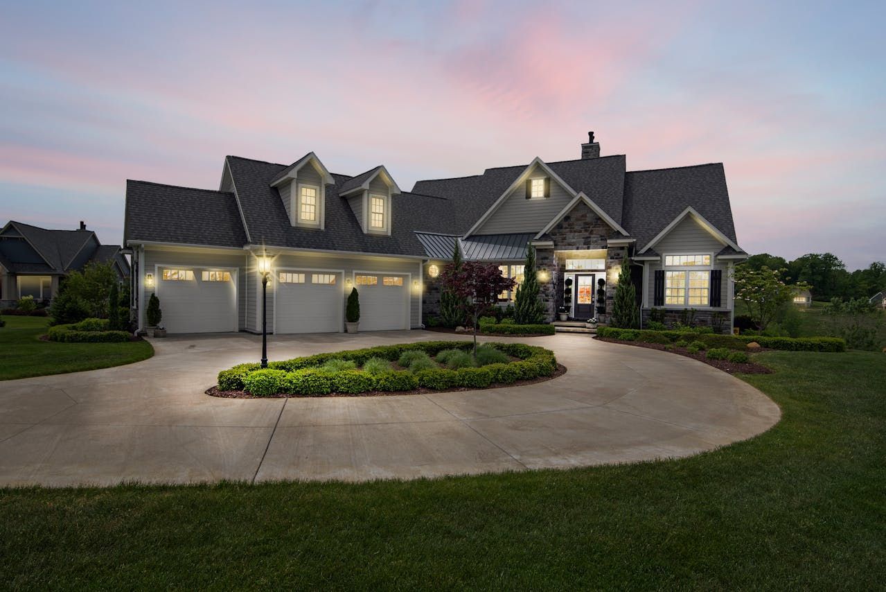 Suburban house at dusk with lit windows, three-car garage, and a circular driveway Suburban house at dusk with lit windows, three-car garage, and a circular driveway
