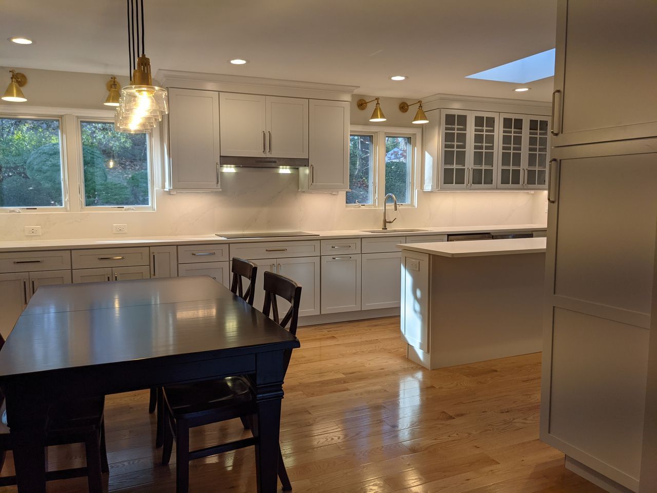 Bright white kitchen with island, dark dining table, hardwood floors, and large windows