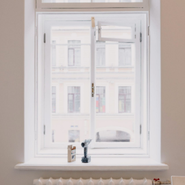 White window with city buildings outside and a small windowsill with a bottle and dark figurine