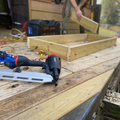 Wooden frame being built on an outdoor workbench with power drill and saw nearby