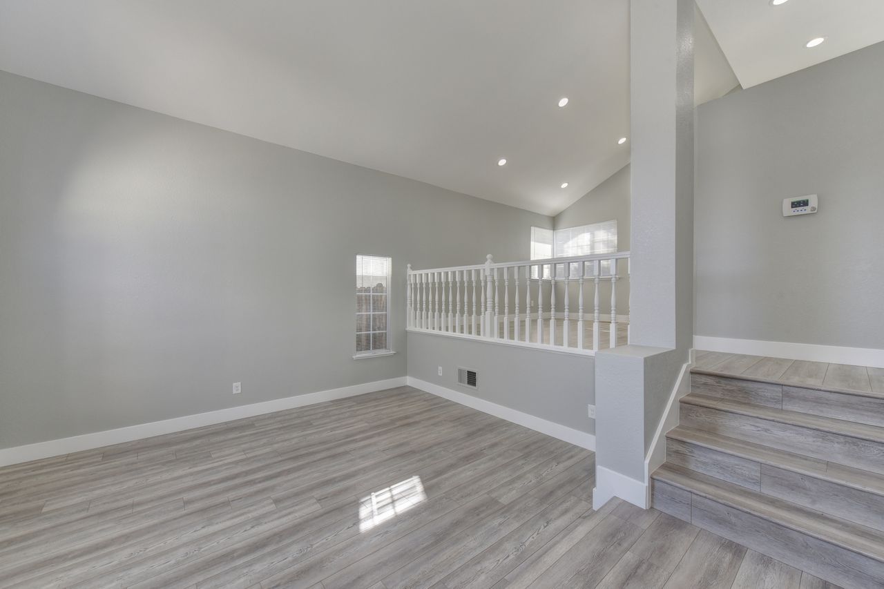 Empty modern living room with gray walls, carpet, stairway, and white railing