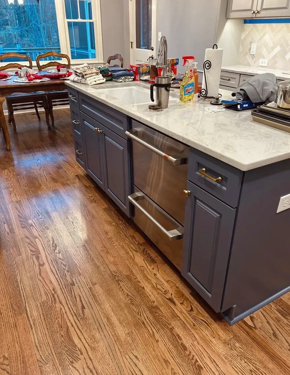 Modern kitchen with dark blue cabinets, stainless appliances, and a light countertop beside a dining area.