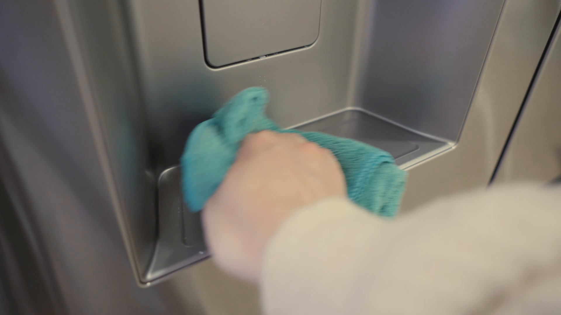 Hand wiping a stainless steel surface with a blue cloth