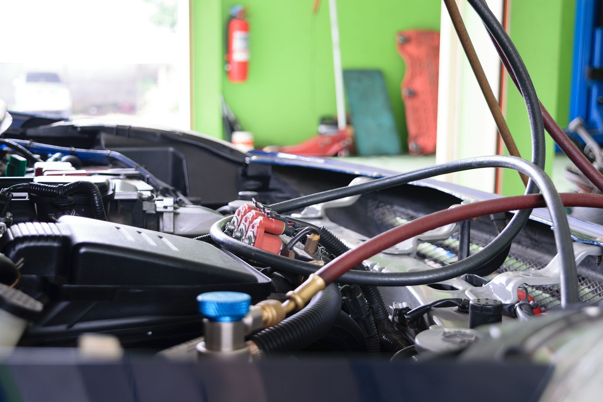 An open car hood in a repair shop with colorful pressure hoses attached to the engine's air conditioning system.