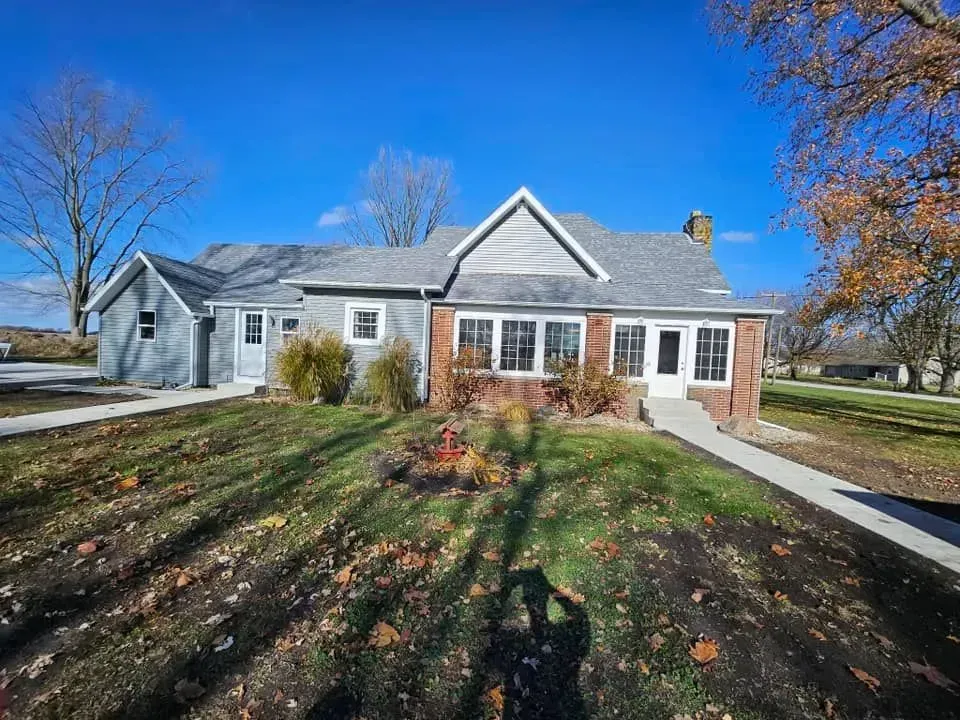 House with gray and brick siding, front yard with grass and trees under a clear blue sky.