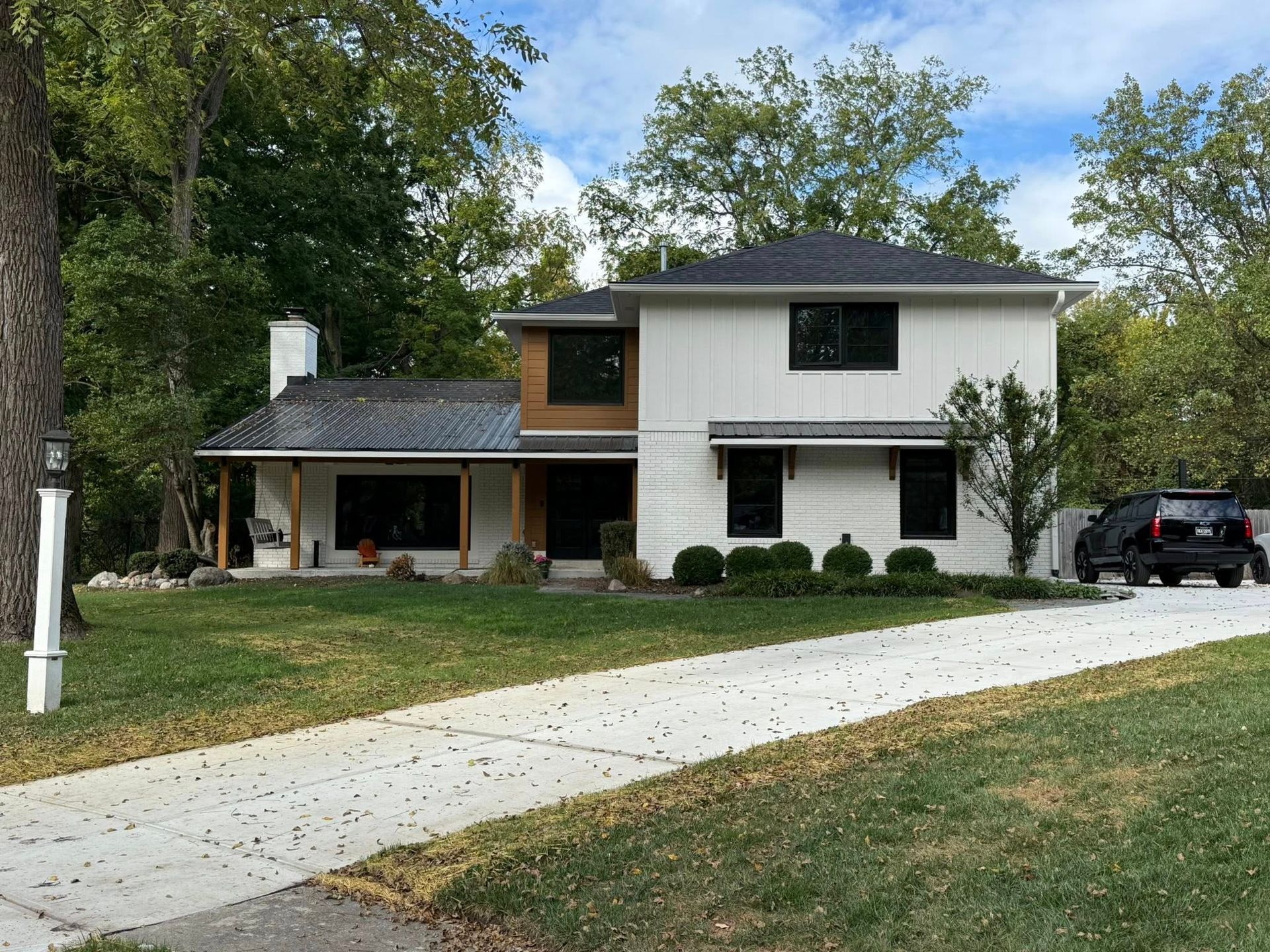 Two-story white house with black trim, brown wood accents, and a concrete driveway.