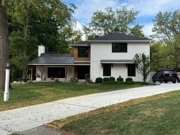 Two-story white house with black trim, brown wood accents, and a concrete driveway.