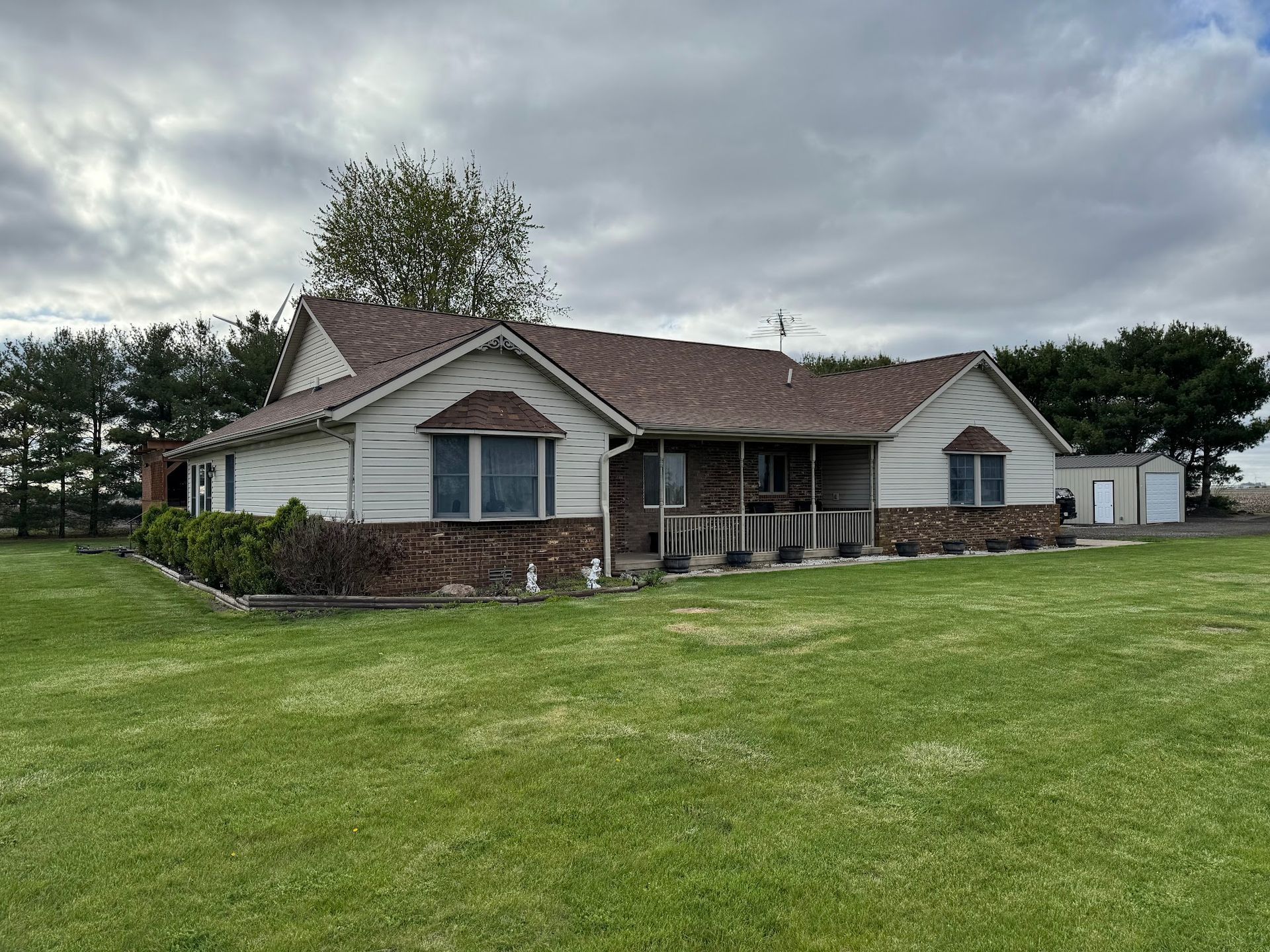 Ranch-style house with brick and siding, brown roof, and a porch, set in a grassy yard under a cloudy sky.