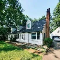A two-story white house with a dark roof and a paved driveway under a blue sky.