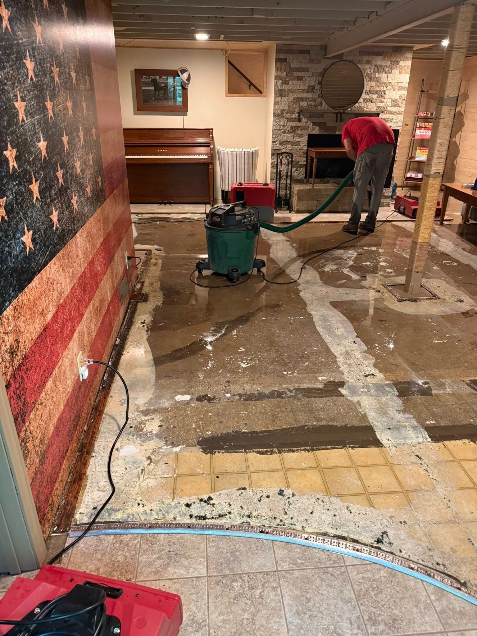 Person using a water vacuum to clean a flooded basement, near an American flag mural.
