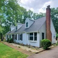 A house with a brick chimney and blue roof, surrounded by trees and a green lawn.