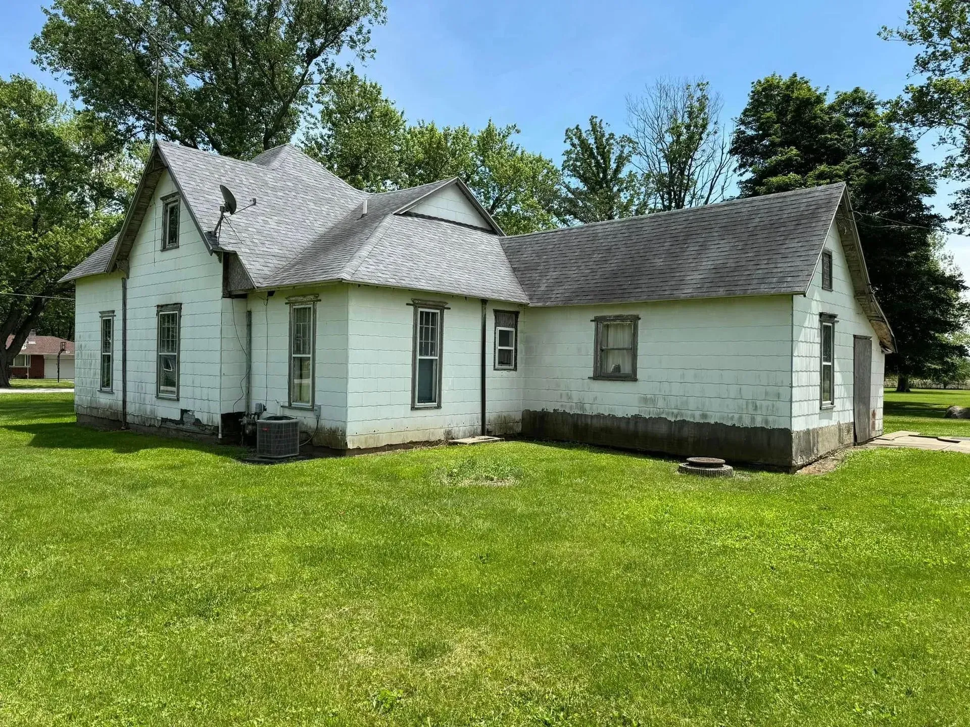 White, two-story house with gray roof, set on grassy lawn, surrounded by trees.