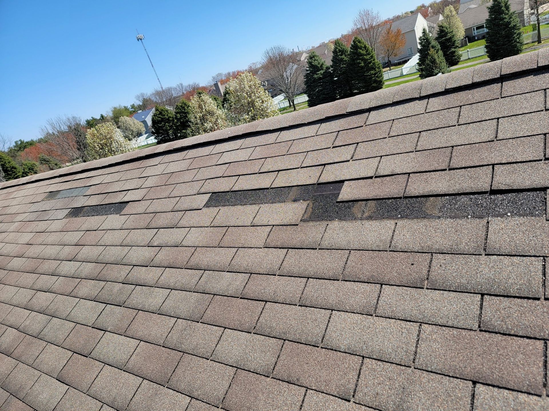 Brown asphalt shingle roof with two areas of missing shingles against a blue sky.