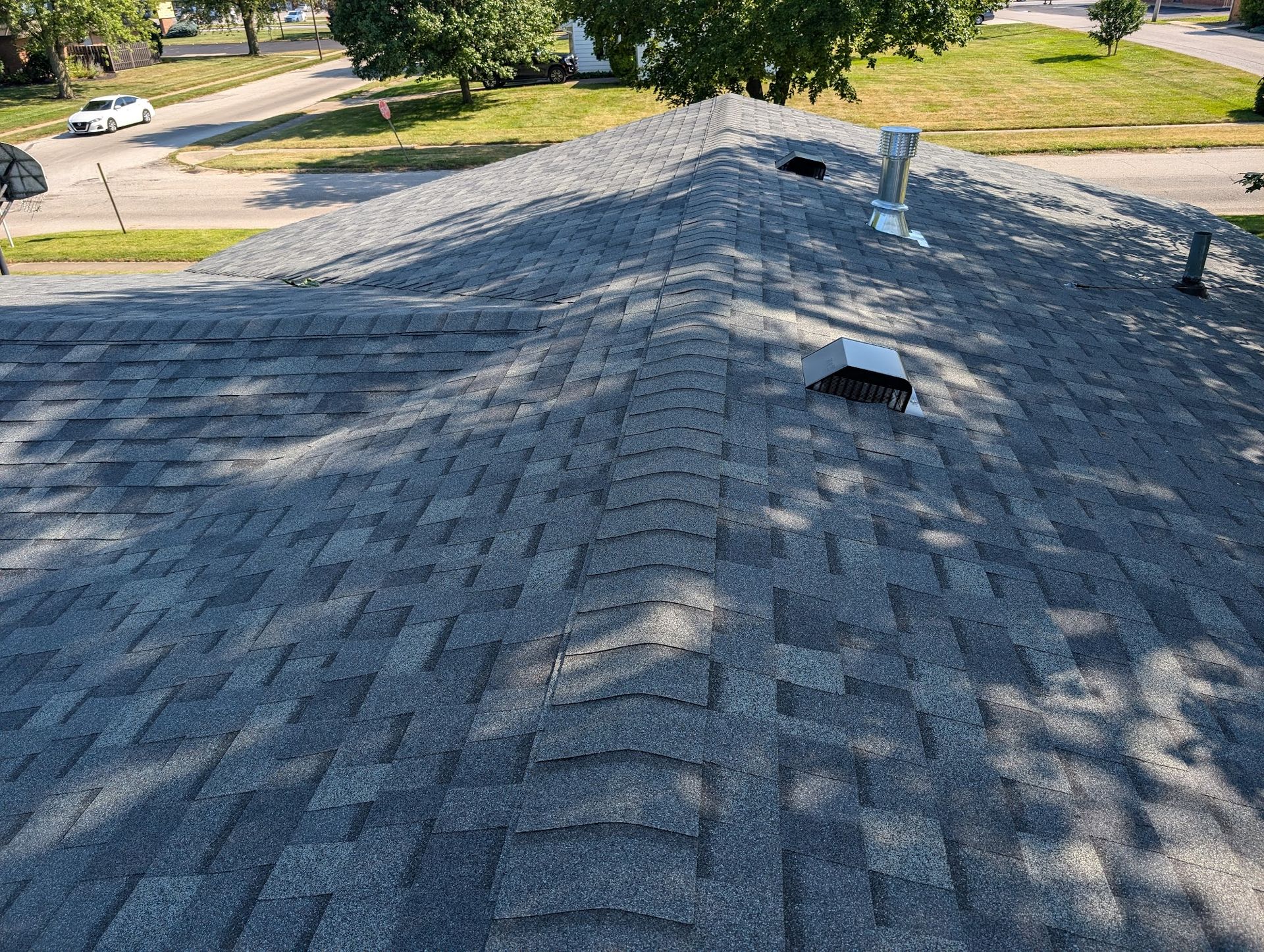Gray asphalt shingle roof, angled view, vents and ridge details visible.