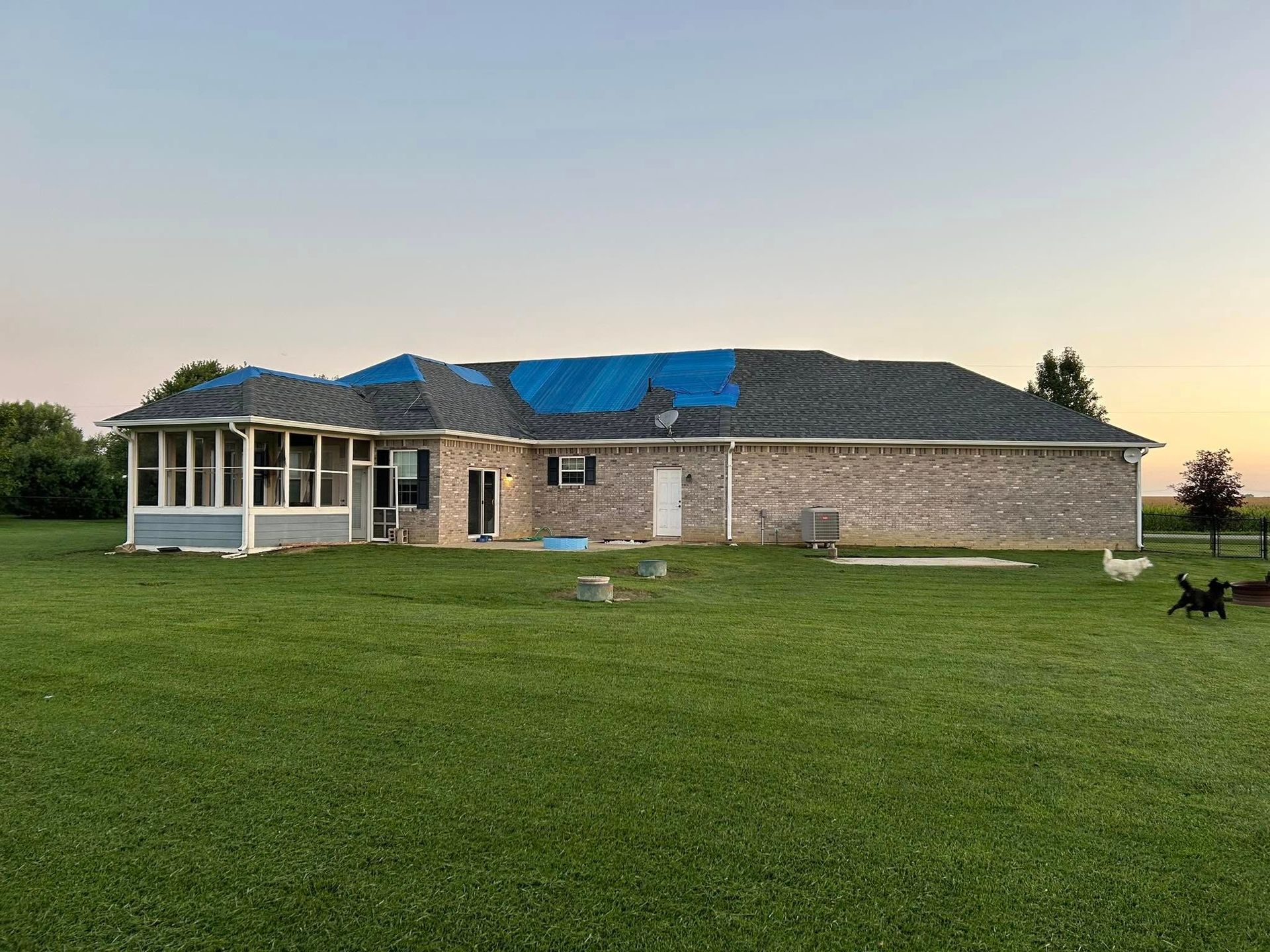 House with partially replaced roof under construction; surrounded by grass at dusk.