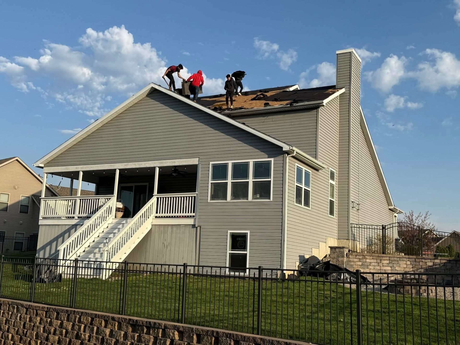 Roofers on a house with gray siding; they're working on the roof under a blue sky.