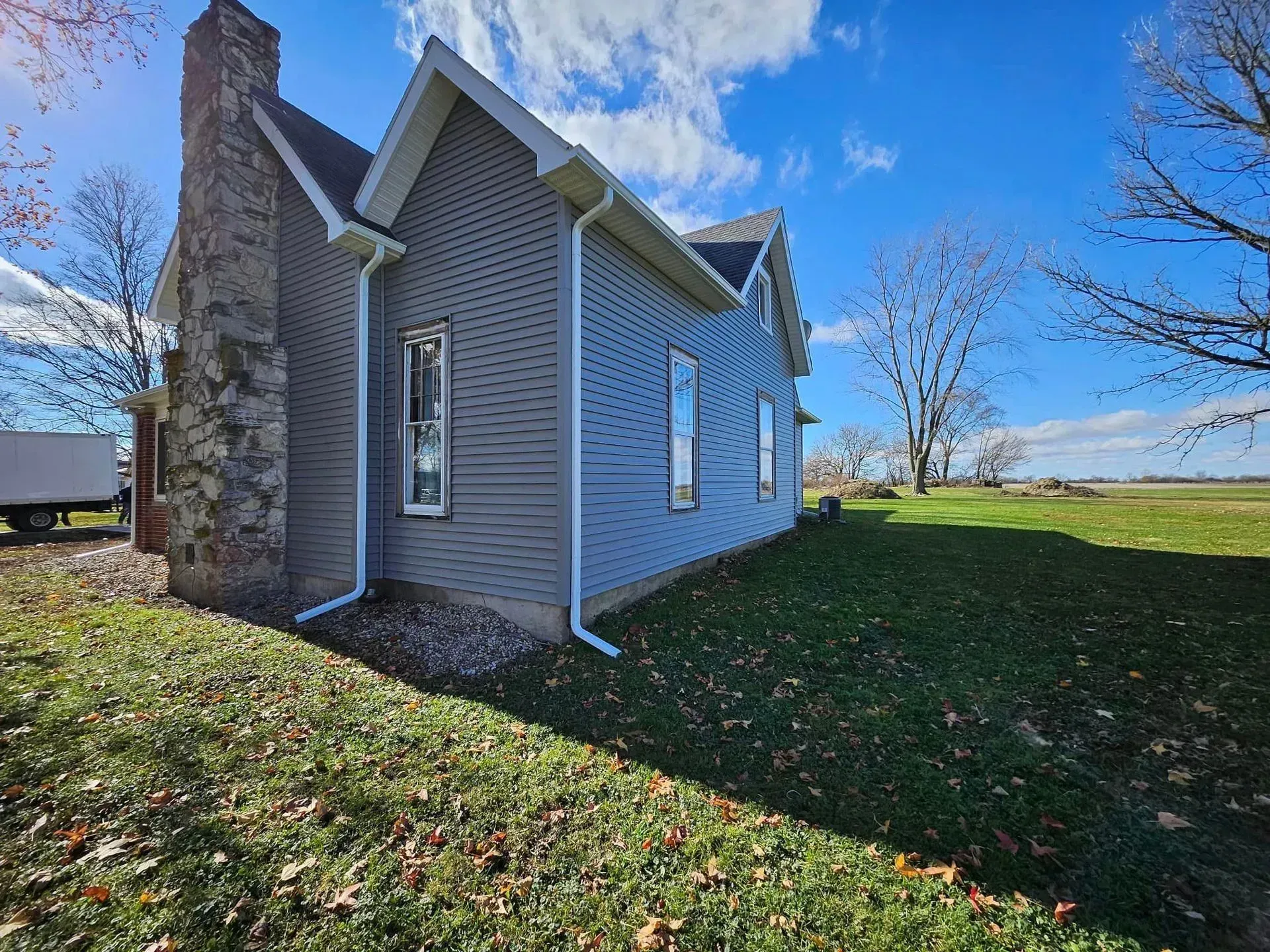 Side view of a blue-sided house with a stone chimney on a grassy lot under a bright blue sky.