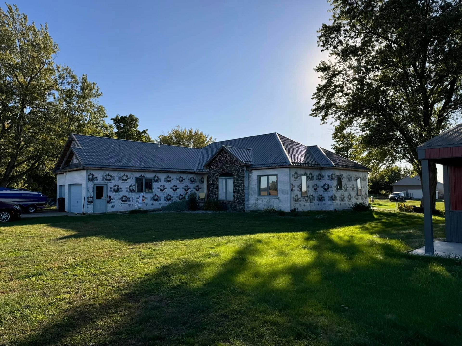 House with a stone facade, unfinished roof, and paper covering the walls, in a grassy yard.