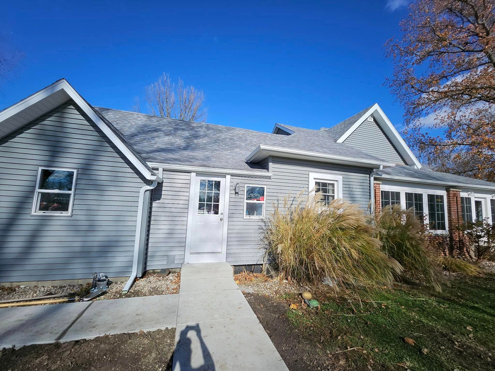 Gray house with a light gray door and roof, blue sky, and a concrete path.