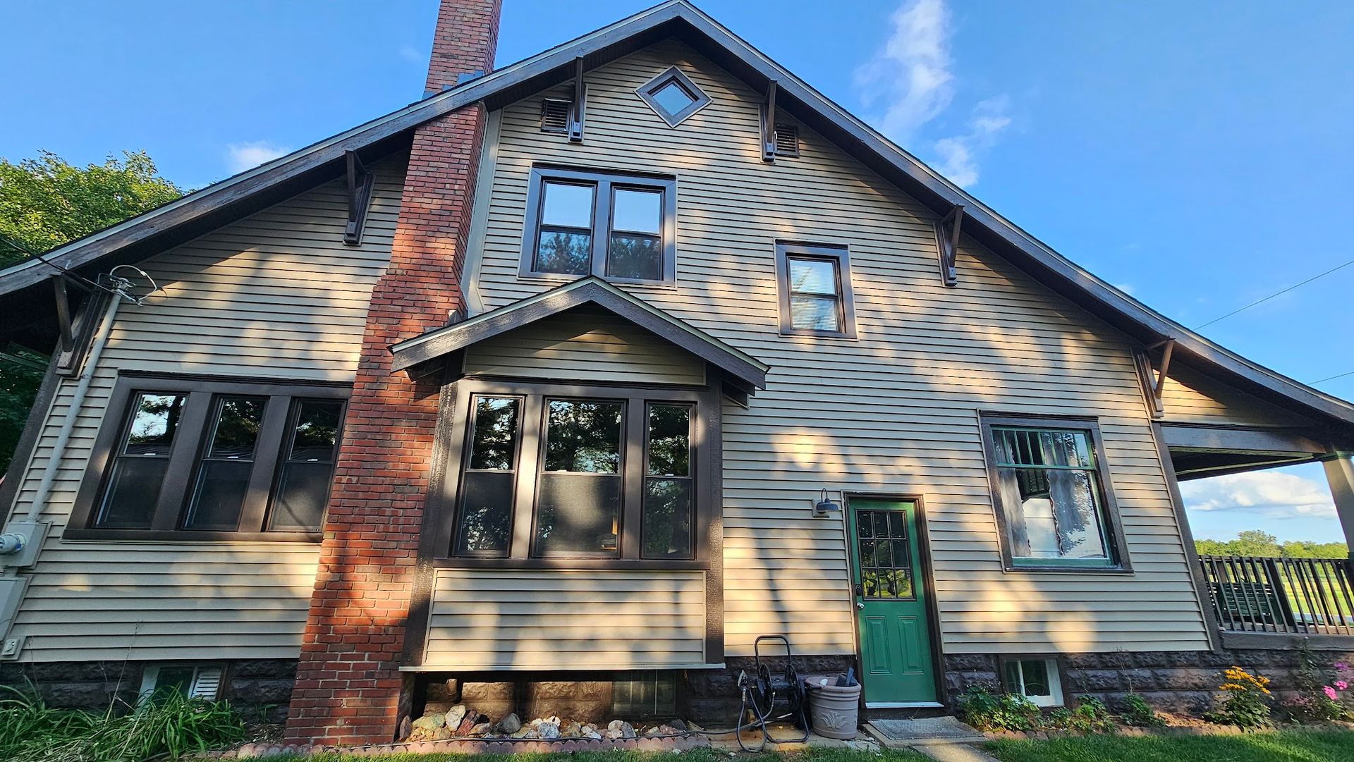 A wooden, two-story house with a brick chimney and green door under a blue sky.