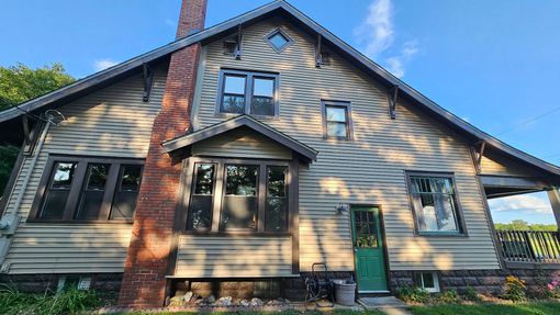 A wooden, two-story house with a brick chimney and green door under a blue sky.
