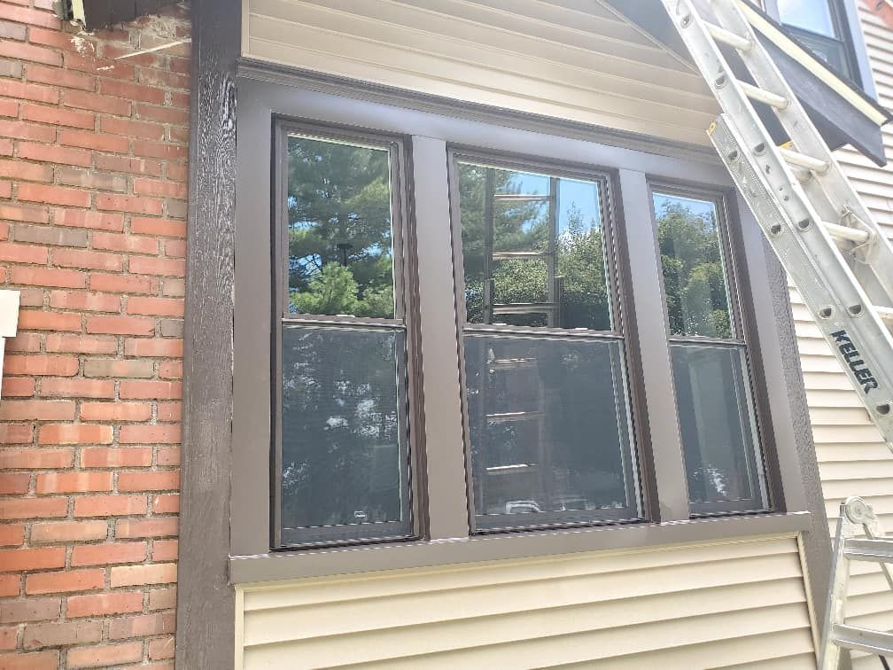 Brown-framed windows on a building with brick and siding; a ladder is leaning against the building.