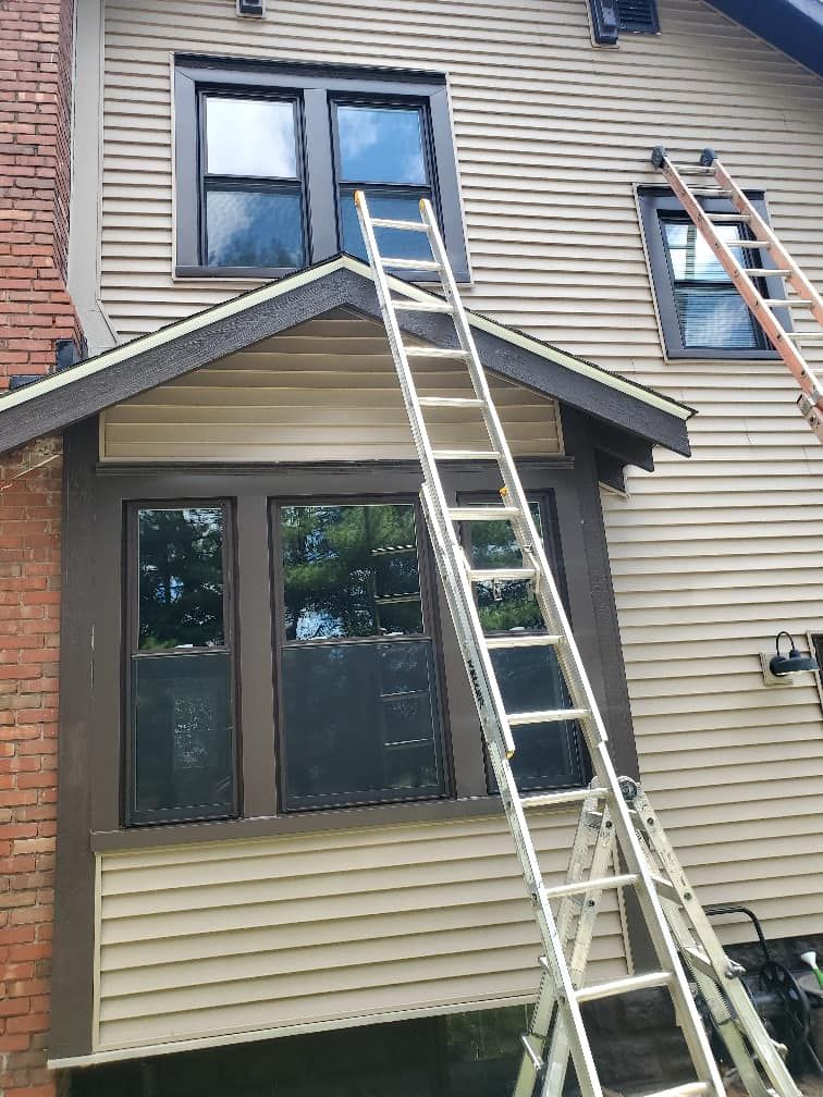A tall silver ladder leans against a two-story house with dark window frames.