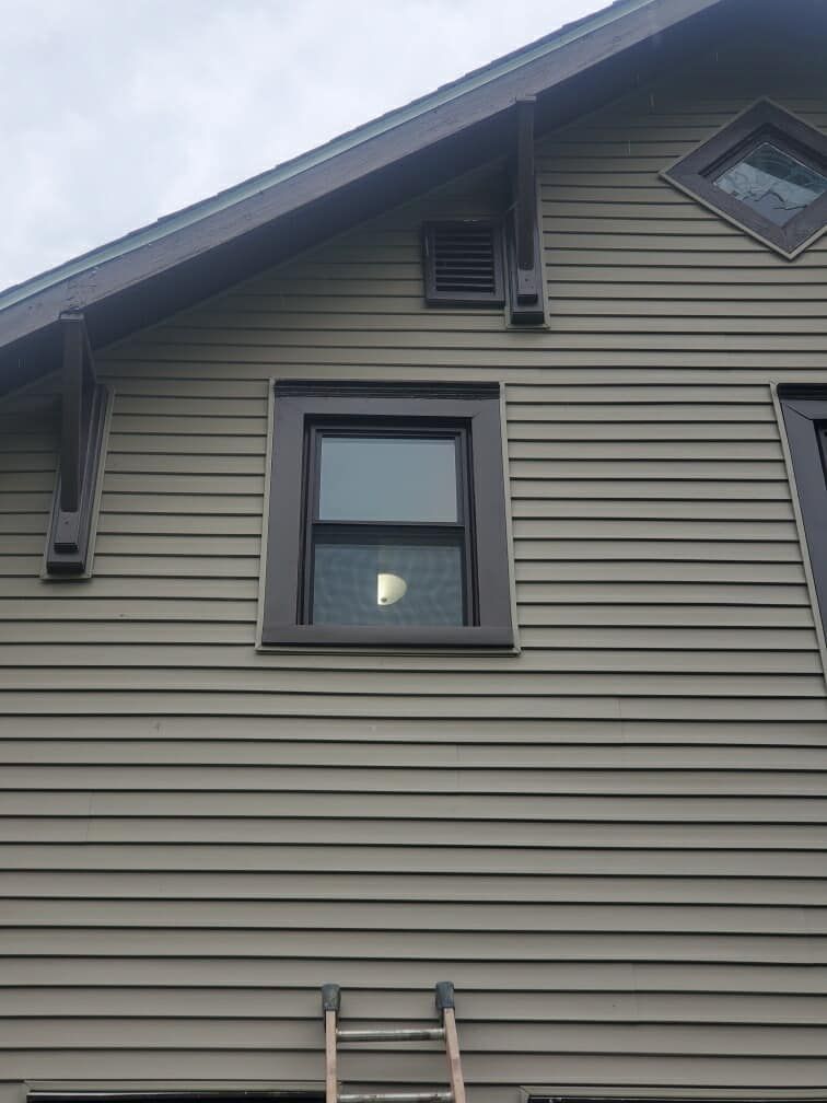 Tan siding on a house with brown trim and windows. A ladder leans against the wall.