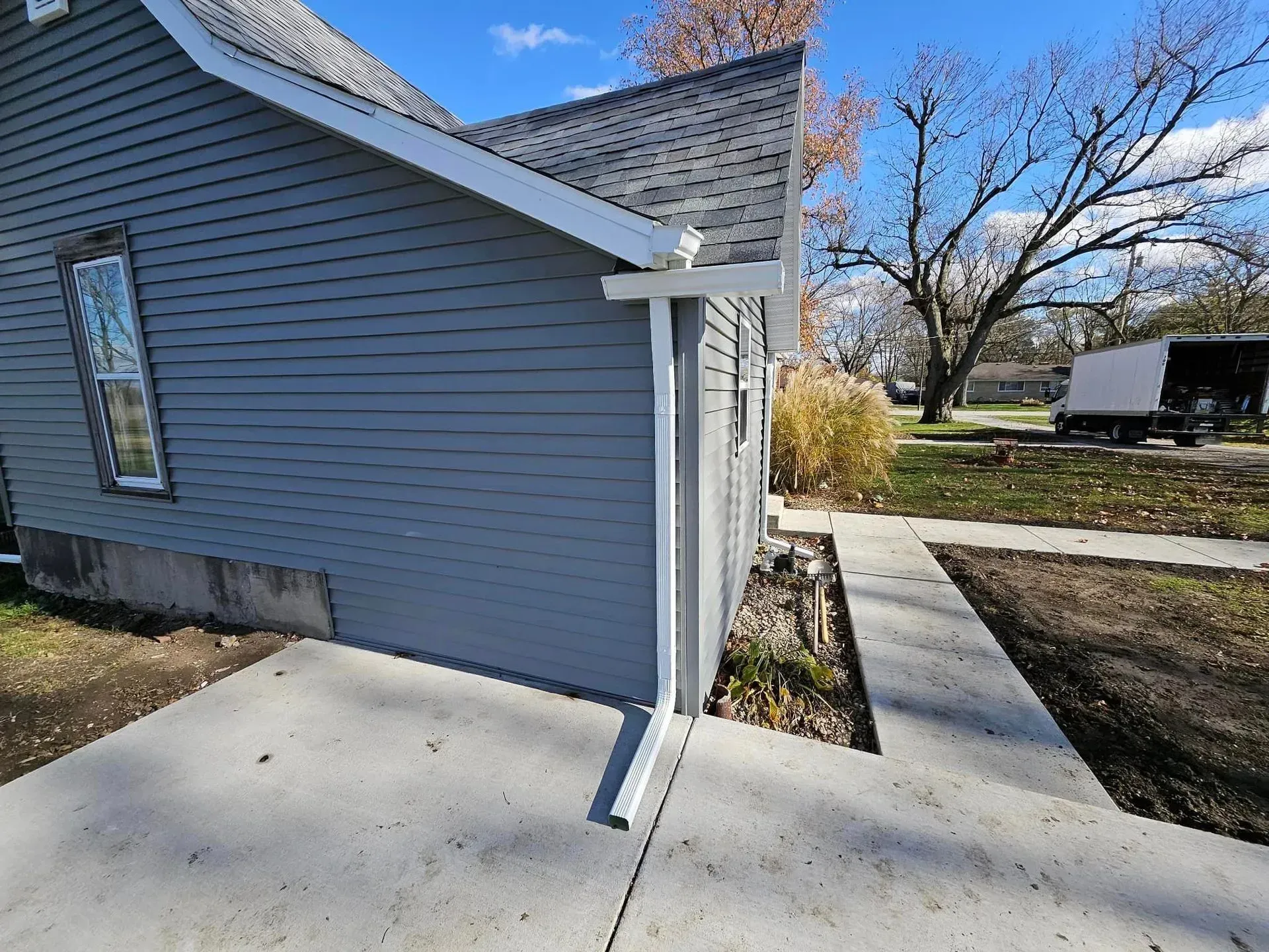 Gray house exterior with white trim, gutter, and a concrete path.