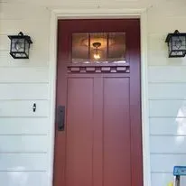 Red front door with glass panel, flanked by black sconces. White siding.