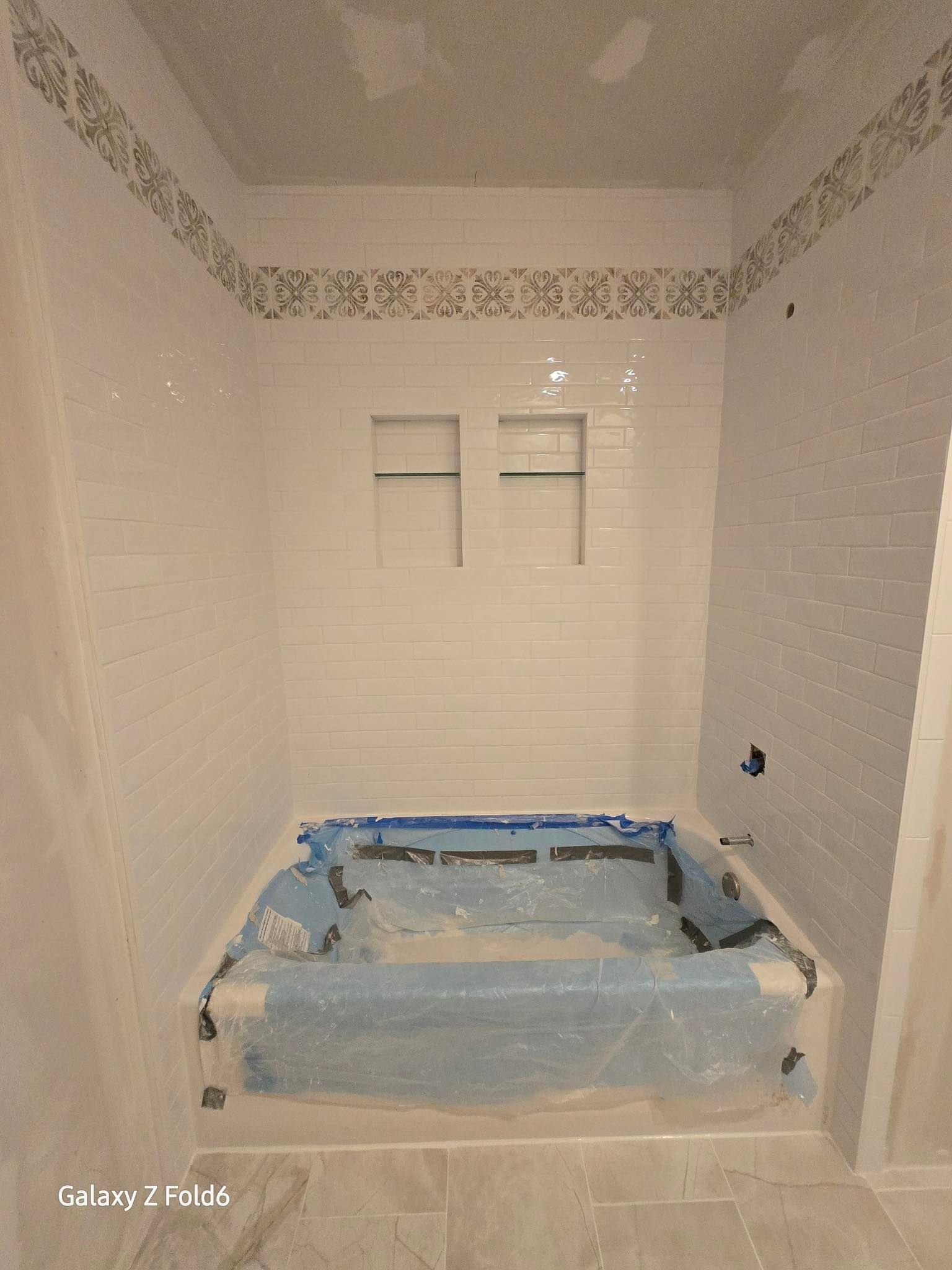 Bathroom remodel with tiled walls, built-in tub, and storage niches.