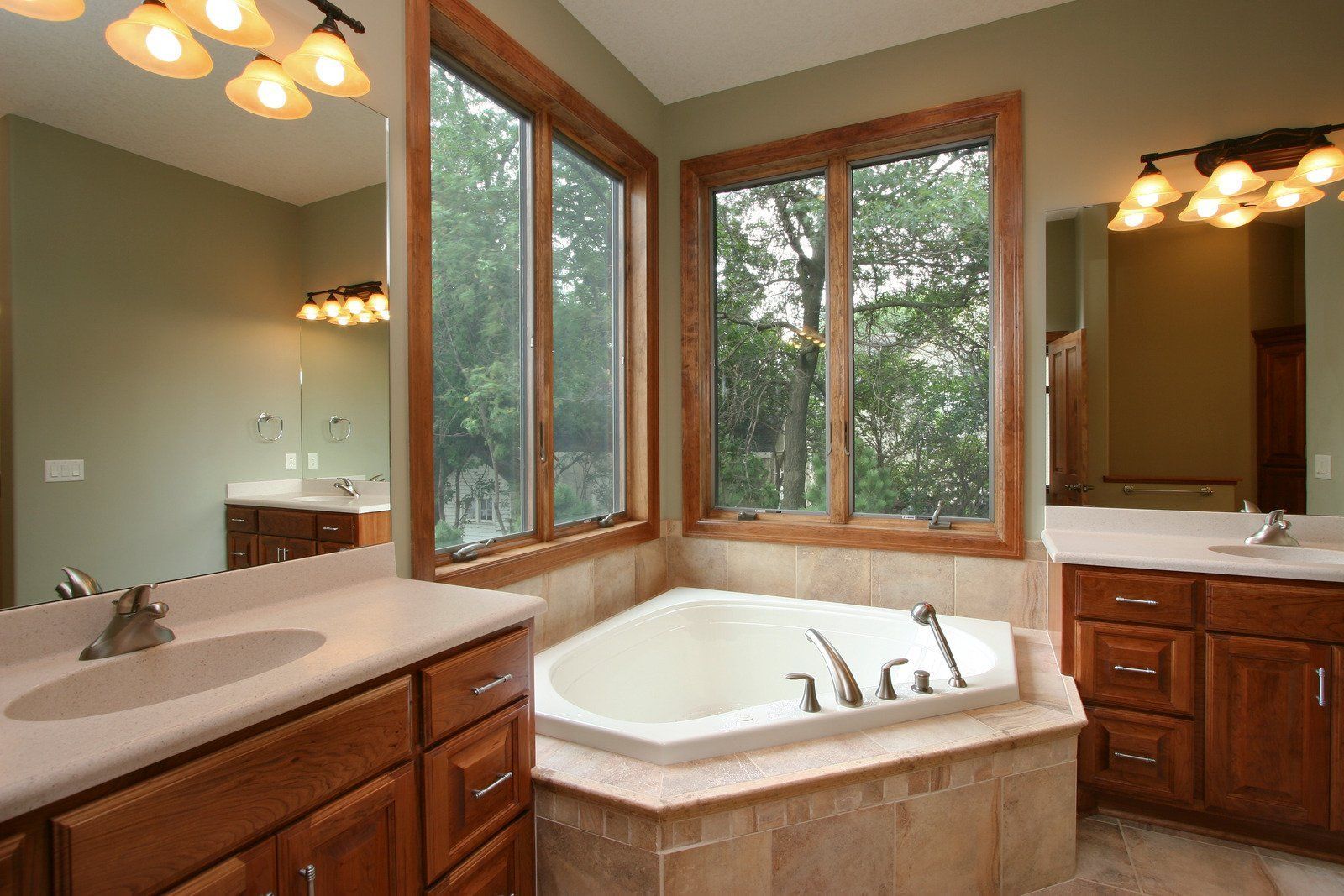 Bathroom with corner jacuzzi tub, windows with wood trim, double vanity, and light fixtures.