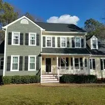 Two-story house with green siding, white trim, and a porch on a sunny day.